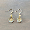 A pair of gold-tone daisy drop earrings with light blue enamel petals, displayed on a dark gray wooden surface.