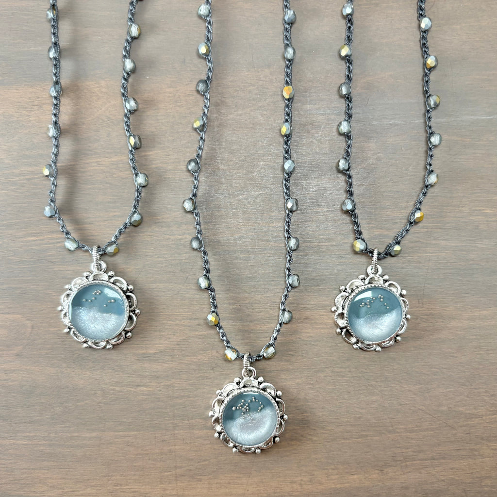 Three beaded necklaces with silver filigree pendants featuring light blue moonstone cabochons, arranged on a brown wooden surface.
