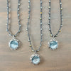 Three beaded necklaces with silver filigree pendants featuring light blue moonstone cabochons, arranged on a brown wooden surface.