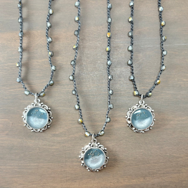Three beaded necklaces with silver filigree pendants featuring light blue moonstone cabochons, arranged on a brown wooden surface.