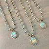 Three gold-toned beaded necklaces with oval turquoise and mountain landscape pendants, arranged diagonally on a gray wood background.