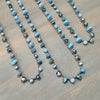 Three beaded necklaces with light blue, white, and dark gray marbled beads on a brown cord, arranged on a gray wood-grain surface.