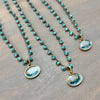 Three beaded necklaces with turquoise-blue marbled stone pendants and bronze-toned chains, arranged diagonally on a brown wooden surface.