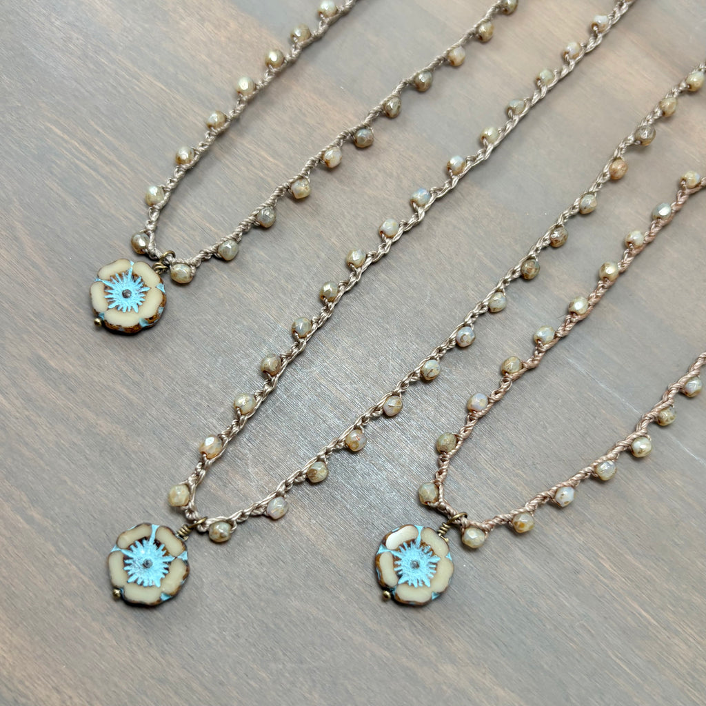 Three beaded necklaces with round floral pendants featuring turquoise centers and gold-toned edges, arranged diagonally on a dark wood surface.