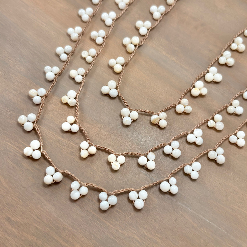 A close-up of a braided brown cord garland decorated with small white beads, arranged in overlapping curved rows on a brown wooden surface.