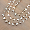 A close-up of a braided brown cord garland decorated with small white beads, arranged in overlapping curved rows on a brown wooden surface.