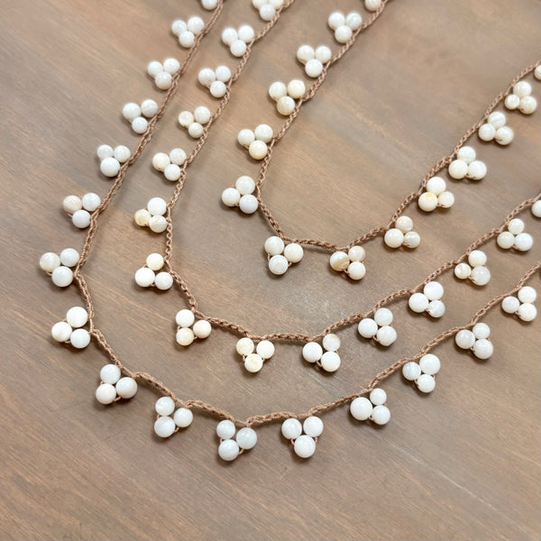 A close-up of a braided brown cord garland decorated with small white beads, arranged in overlapping curved rows on a brown wooden surface.