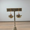 A pair of handmade daisy earrings with bronze-toned petals, a central brown pearl, and gold hooks, displayed on a burlap-covered jewelry stand against a neutral gray background.