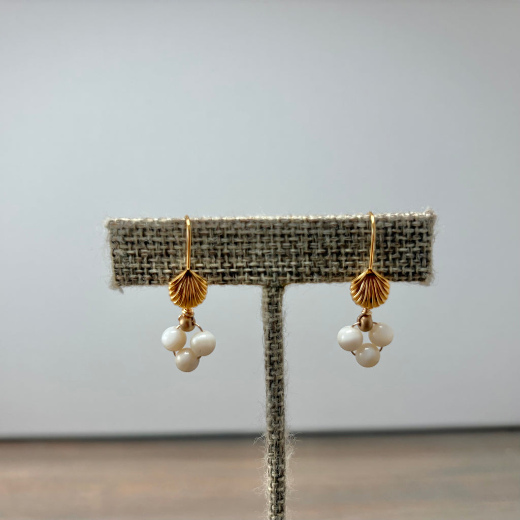 A pair of gold and white pearl dangle earrings displayed on a textured fabric jewelry stand against a plain light gray background.