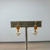 A pair of gold and white pearl dangle earrings displayed on a textured fabric jewelry stand against a plain light gray background.