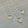 Three gold fairy luna moth necklaces with  small white pearl-like beads on a textured gray wooden surface.