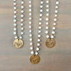 Three bohemian-style beaded necklaces with white round beads and antique bronze butterfly coin pendants, arranged on a brown wooden surface.