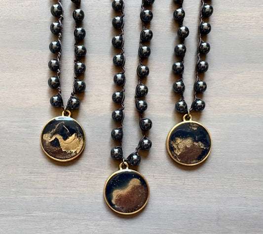 Three black beaded necklaces with gold and brown pendant stones on a light wooden surface.