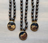 Three black beaded necklaces with gold and brown pendant stones on a light wooden surface.
