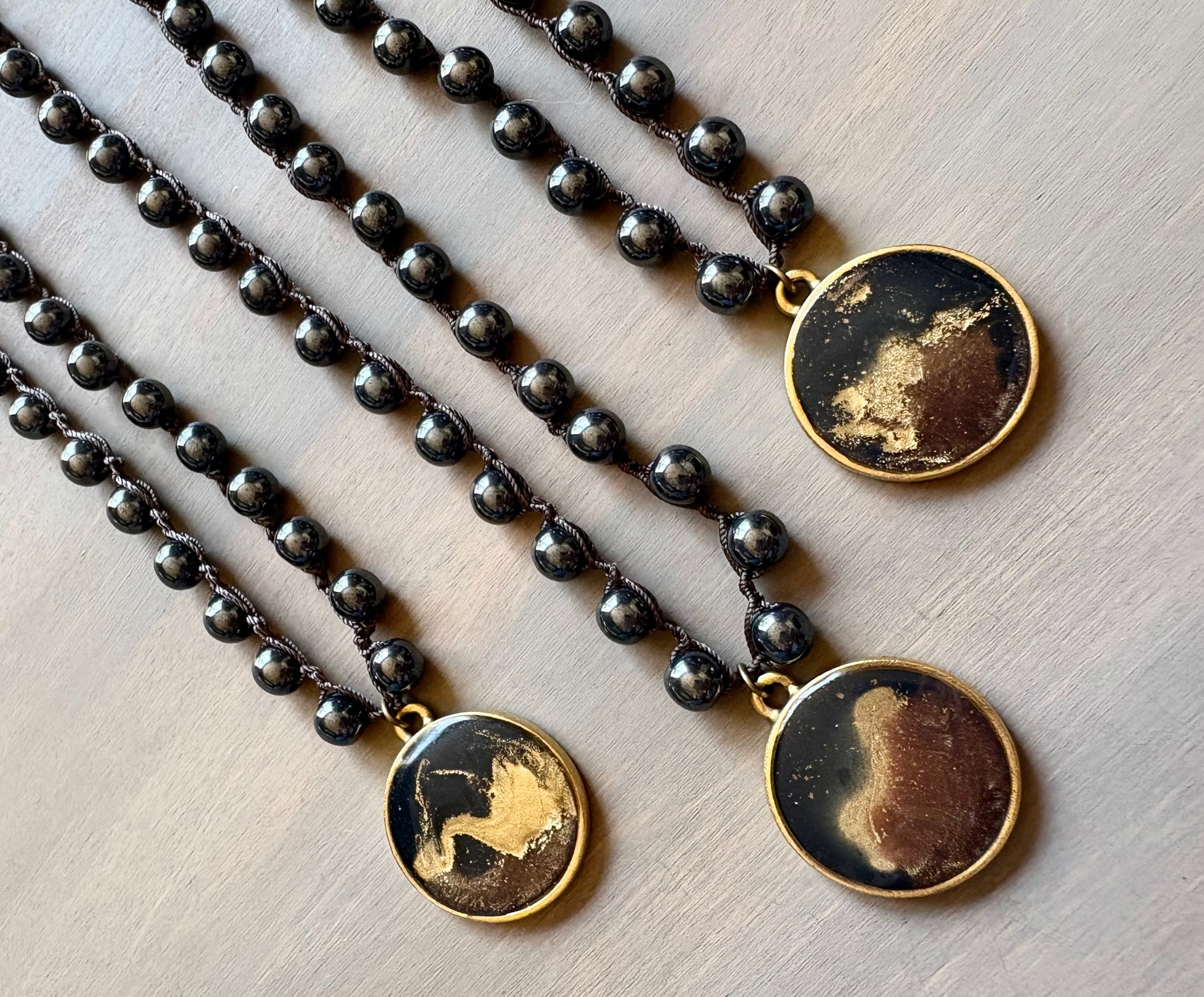 Three black beaded necklaces with gold pendant stones on a light wooden surface